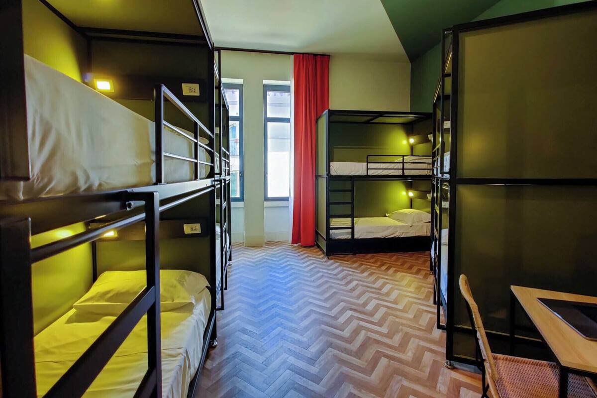 Une chambre de dortoir avec des lits superposés, un plancher en bois et un rideau rouge.