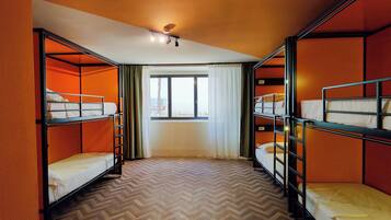 A dormitory room with bunk beds, a window with curtains, and a herringbone-patterned floor.