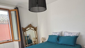 Ett sovrum med en säng, en spegel, ett fönster och en hängande lampa.