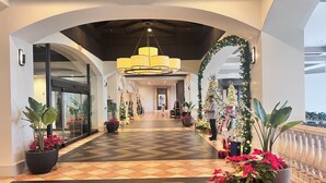 Un pasillo de hotel con piso estampado en diseño de chevrón, plantas grandes en macetas, árboles de Navidad y una lámpara de araña moderna.