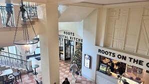 Un espacio interior amplio con piso a cuadros, una lámpara colgante y un restaurante llamado 'Roots on the Coast'.