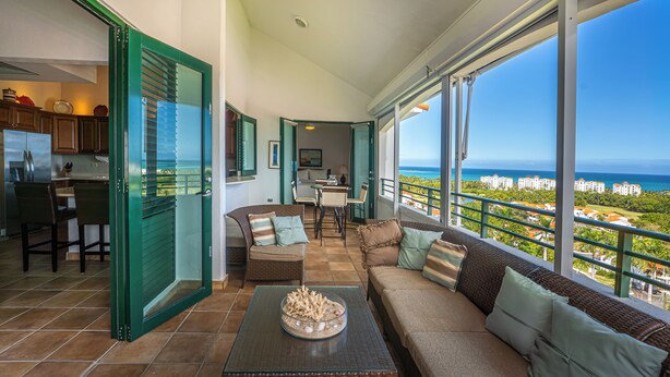 Amplia sala de estar con un ventanal que ofrece vistas a la costa, un comedor y una cocina con refrigerador.