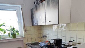 Eine kleine Küche mit weißen Schränken, einer schwarzen Arbeitsplatte und einem Fenster mit Blumentöpfen.