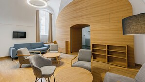 A modern interior with a blue sofa, grey armchairs, and a wooden bookshelf. - Hotel Benedict (Koszeg)