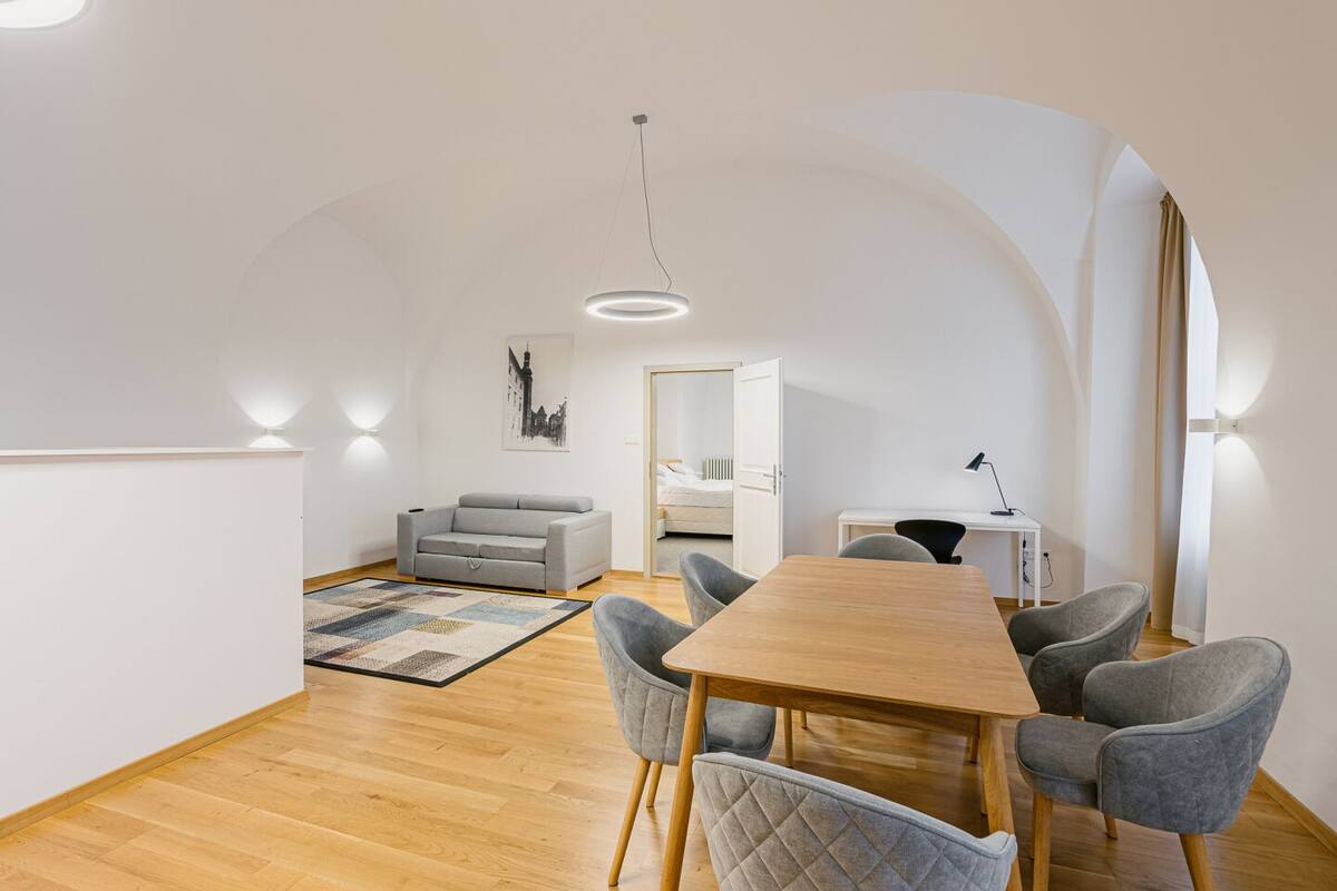Un espacio habitable y comedor moderno de concepto abierto, con una mesa de madera, sillas tapizadas en gris, un sofá gris y una alfombra estampada.