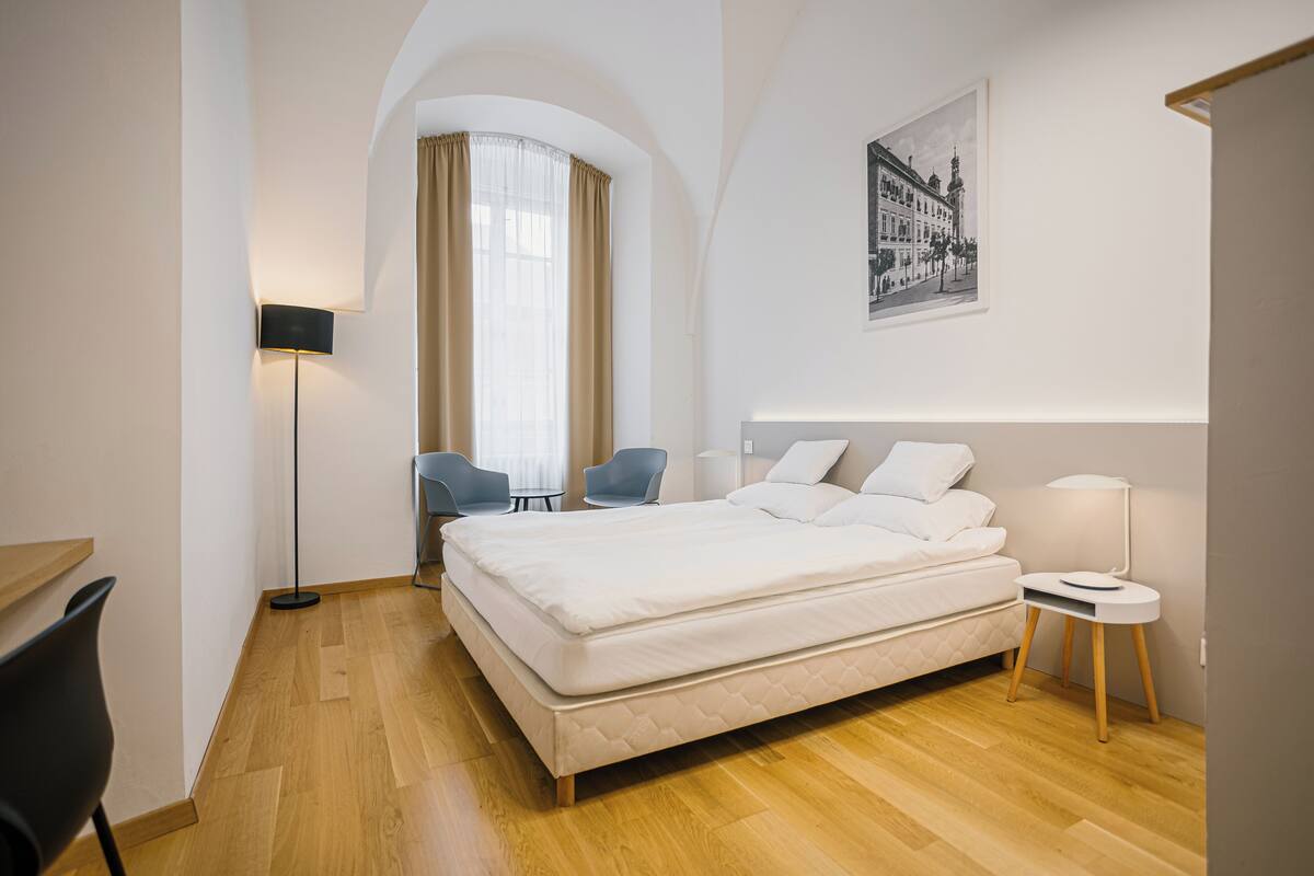Una habitación de hotel moderna con una cama grande, un escritorio, una silla, una mesita y una lámpara.