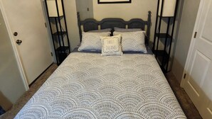 Un dormitorio con una cama, un ventilador de techo, un cuadro enmarcado en la pared y dos mesitas de noche.