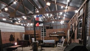 Un interior de estilo industrial con paredes de ladrillo visto, suelo de hormigón y un techo alto con vigas metálicas. Se observan mesas y sillas de madera, una pequeña barra y una escalera que lleva a un nivel superior.