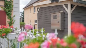 Een woongebouw met een grijze gevel, een witte hek en bloeiende planten.