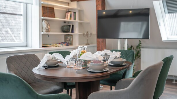 Een eetruimte met een ronde tafel voor vier personen, omringd door groene fauteuils.