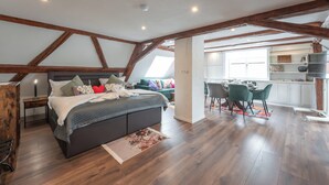 Een slaapkamer met een groot bed, een bureau en een stoel in een kamer in loftstijl met zichtbare houten balken.