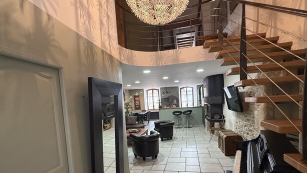 A spacious living area with a piano, a staircase, and a kitchen in the background. - Spacious apartment in cévenol village house (Barre-des-Cévennes)