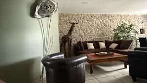 A living room with a stone wall, a giraffe sculpture, a brown sofa, and a black leather chair. - Spacious apartment in cévenol village house (Barre-des-Cévennes)