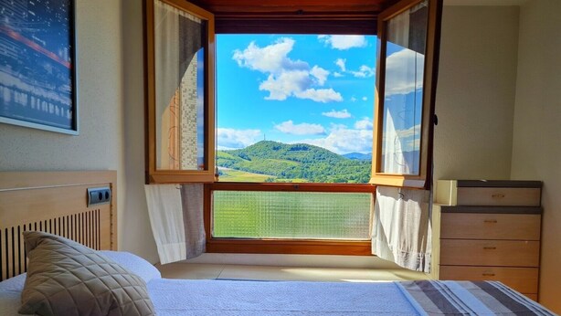 Un dormitorio con cama, cómoda y ventana con vistas a las colinas verdes.
