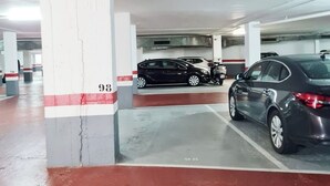 Un estacionamiento con pilares de hormigón, suelo rojo y varios coches aparcados.