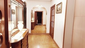 Un pasillo con suelo de madera, un espejo, un aparador y una puerta que da a otra habitación.