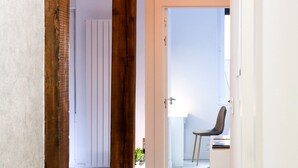 A hallway with a wooden door, a white door, and a chair in a room with a white wall and a window. - Apartamento Kursal by SanSe Holidays (Donostia)