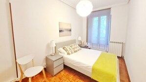 A bedroom with a bed, bedside tables, a chair, a window, and a painting on the wall. - Apartamento Urbieta by SanSe Holidays (Donostia)
