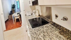 A compact kitchen with white cabinets, a granite countertop, a built-in oven, and a small dining area with a chair and table. - Apartamento Urbieta by SanSe Holidays (Donostia)