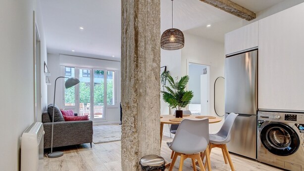 A modern kitchen with a built-in washing machine, a dining area with a table and chairs, and a large window offering a view of the outdoors. - Gran Vía Arena by SanSe Holidays (San Sebastián)