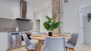 A modern kitchen with a stainless steel dishwasher, oven, and a tall chimney. There is a dining table with four chairs and a potted plant. - Gran Vía Arena by SanSe Holidays (San Sebastián)