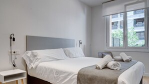 A modern hotel room with a neatly made bed, a bedside table, and a window with a view of the building outside. - Gran Vía Arena by SanSe Holidays (San Sebastián)
