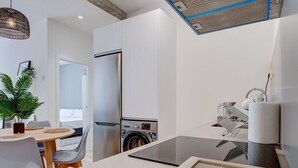 A modern kitchen with a built-in washing machine, a refrigerator, and a dining area with a table and chairs. - Gran Vía Arena by SanSe Holidays (San Sebastián)