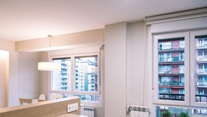 Une cuisine moderne avec un coin repas, de grandes fenêtres et une vue sur un immeuble d’habitation.