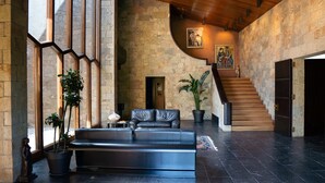 Un hall d’entrée spacieux, avec un canapé en cuir noir, des murs en pierre et un escalier en bois.