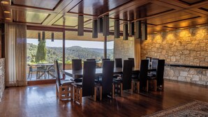 Un vaste espace dédié à la salle à manger, avec une grande table et des chaises, un mur en pierre et une vue sur l’extérieur.