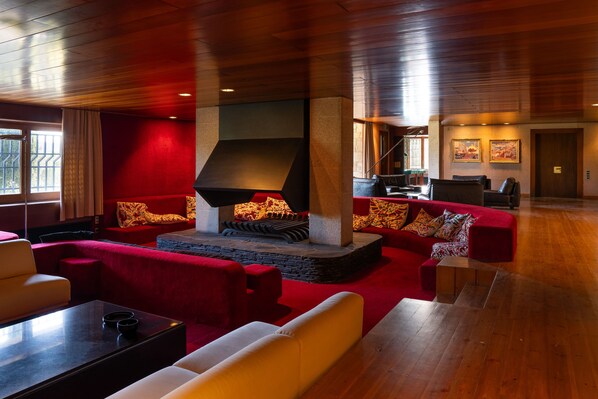 A spacious living area with a fireplace, red and white sofas, a coffee table, and wooden flooring.