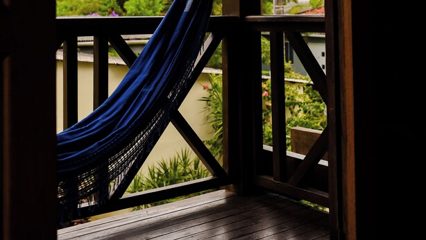 Un hamac sur une terrasse en bois, avec vue sur la verdure et un palmier.