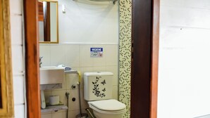 Une salle de bain équipée de toilettes, d’un lavabo et d’une douche. Un panneau indiquant les règles d’hygiène est affiché sur le mur.