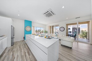 A modern kitchen with a central island, a white sofa, and a large window with a view of palm trees.