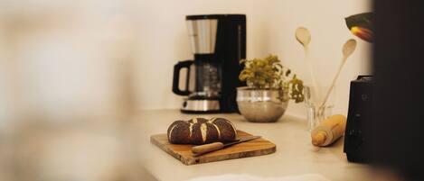 Eine Küchenarbeitsplatte mit Brot, einer Kaffeemaschine, einer Schüssel mit Besteck und einer Pflanze.