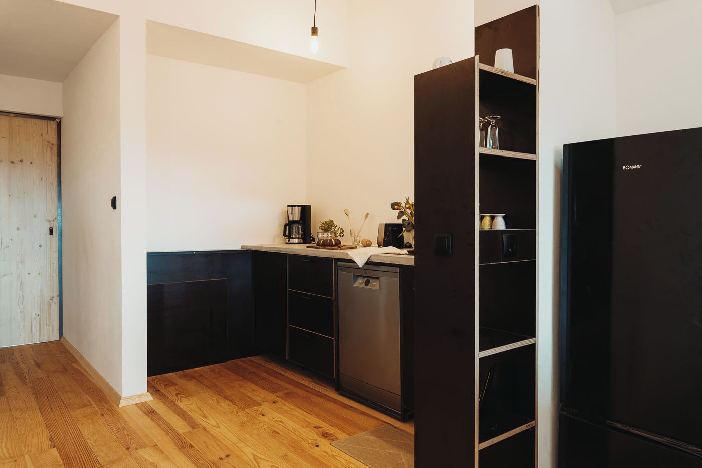 Een compacte keuken met donkere kastjes, een vaatwasser en een koffiezetapparaat op het aanrecht.