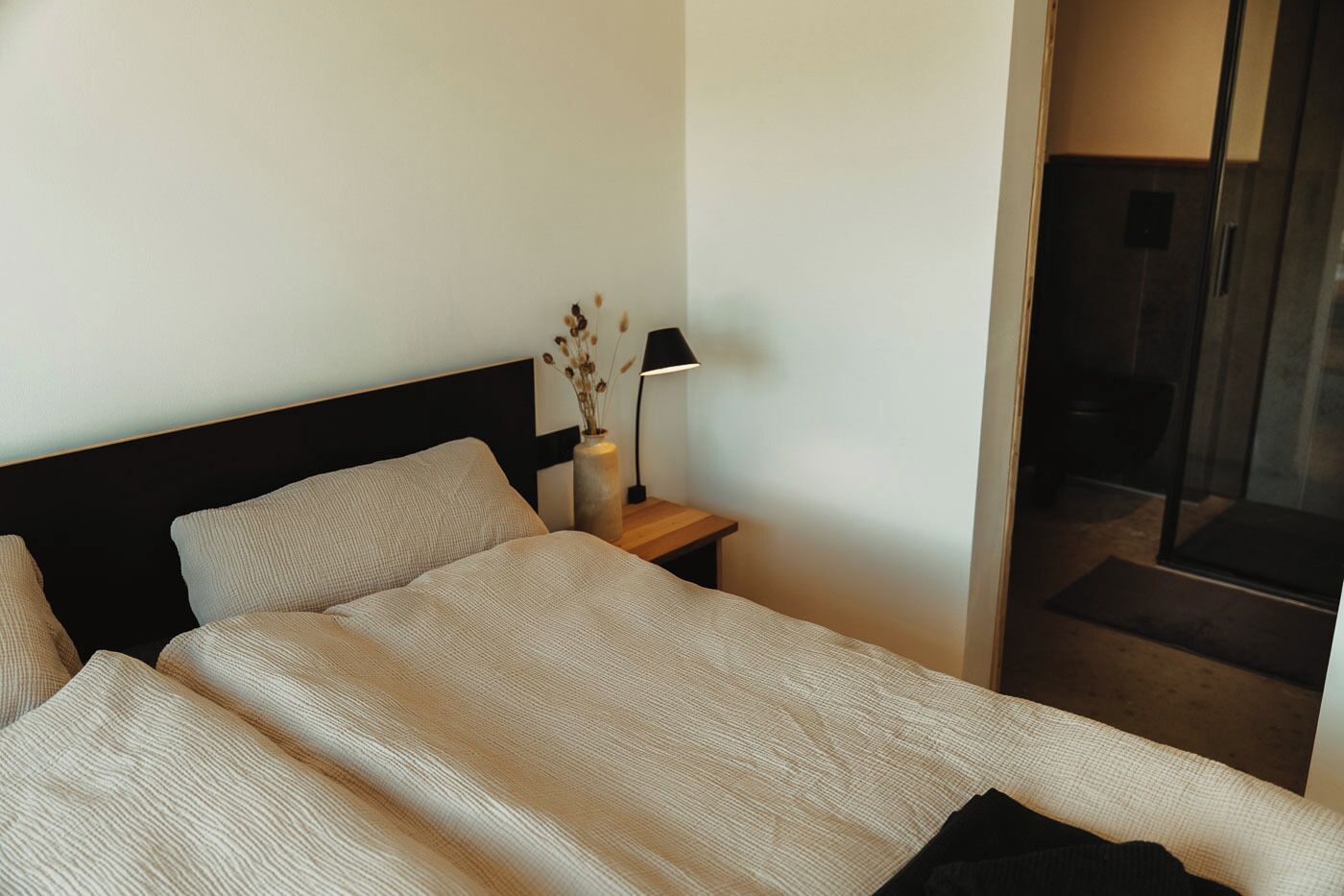 Ett modernt hotellrum med en stor säng, ett nattduksbord med en lampa och utsikt över omgivningarna genom en glasdörr.