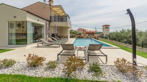 A modern villa with a swimming pool, outdoor seating, and a view of the surrounding landscape.
