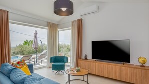 A modern living room with a large TV, a sofa, a small table, and a balcony with a pool.