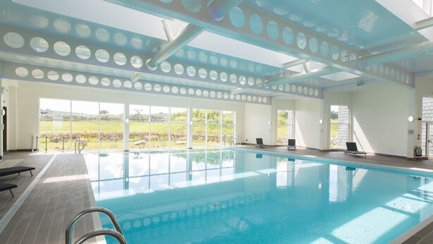 An indoor swimming pool with clear views of the outdoors, a tiled floor, and a metal ladder.