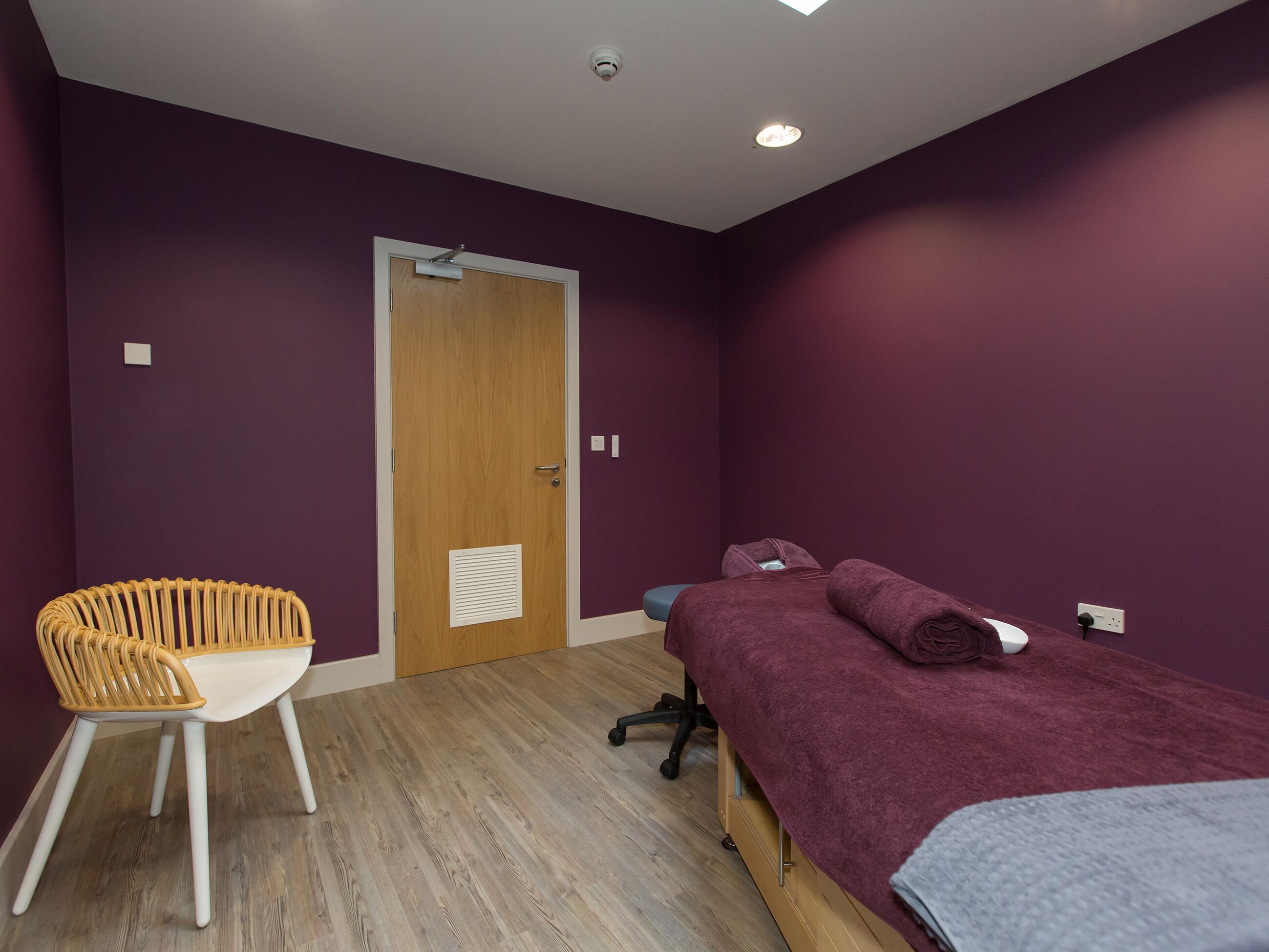 Een kamer met een bed, een stoel, een deur en een plafondlamp.