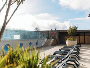 A rooftop terrace with a row of sun loungers, a potted plant, and a staircase leading to a wooden building.