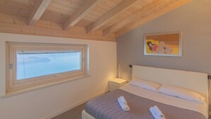 A bedroom with a bed, a nightstand, a lamp, a window with a view, and a painting on the wall.