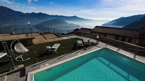 A pool with clear water, surrounded by a deck with chairs and tables, overlooking a mountainous landscape.