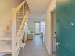 Un escalier menant à un balcon, un canapé blanc, une table et une porte de couleur turquoise.