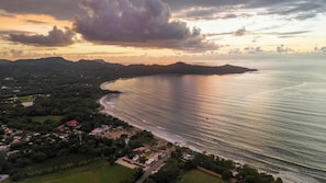 An aerial view of a coastal area with a beach, residential buildings, and a mountainous backdrop. - Suite 3 - Jaguar Beach & Pool 2 BR Condo (Brasilito)
