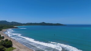 Eine Küstenlandschaft mit Strand, klarem blauen Meer und grünen Hügeln im Hintergrund.