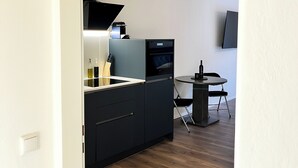 Une cuisine moderne avec des meubles de couleur sombre, un four encastré et un four à micro-ondes. On y trouve également un coin repas avec une table ronde et des chaises.