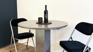 Une table ronde avec un pied en métal, deux chaises noires et une bouteille de vin posée sur la table.