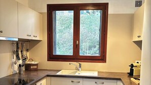 A modern kitchen with white cabinets, a double sink, and a window with a view of greenery. - Villa Laurier U Benedettu (Lecci)